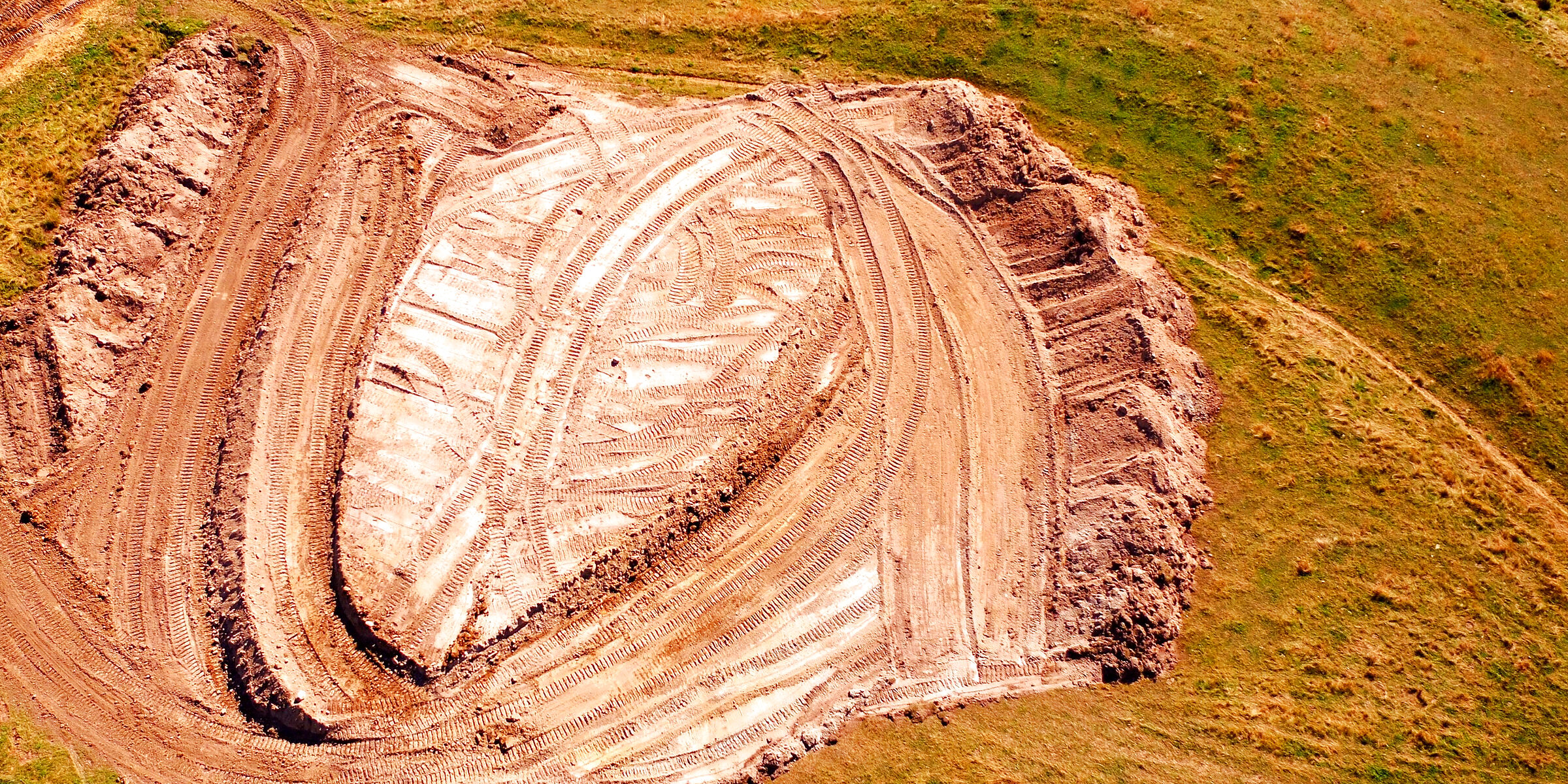 A borrow pit seen straight down from the air: the cut floor, the benches and ramps around it and the overlapping passes of the machines that cut it.
