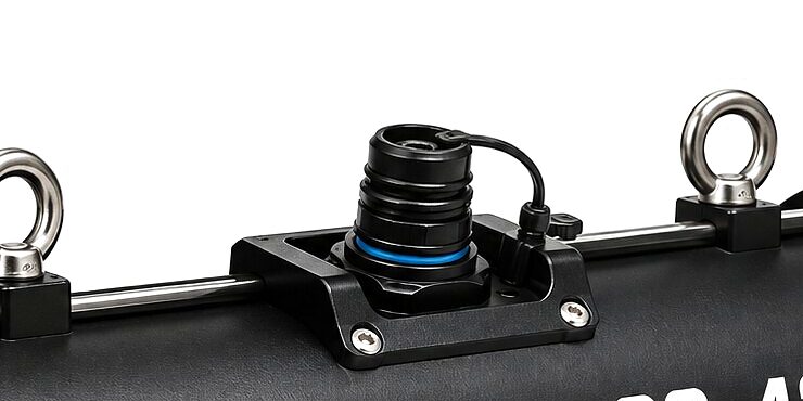 The top of the CS-430 close in: the fibre port on its mounting plate, its dust cap hanging on a tether, between two lifting eyes on the side rail.